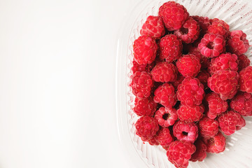 Close-up ripe juicy and delicious raspberry in a plastic transparent dish on a light background. Saturated healthy food
