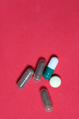 Gelatin pills and tablets of different colors. Medicines scattered on the background of coral color.