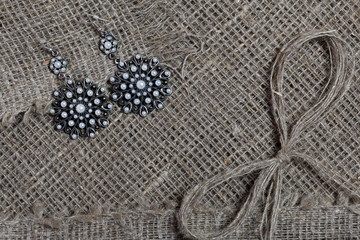 Coarse linen fabric. On it are earrings with pebbles and a bow of linen threads.