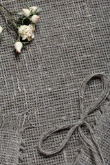 Coarse linen fabric. On it are dried beige roses and a bow of linen threads.