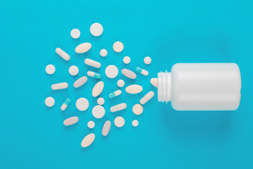 Assorted pharmaceutical medicine pills, tablets and capsules and bottle on blue background. Copy space for text