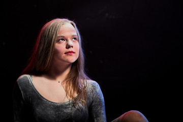 Portrait of young teen girl in a dark room after photoshoot with flour with a colored light and a black background