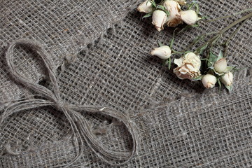 Coarse linen fabric. On it are dried beige roses and a bow of linen threads.