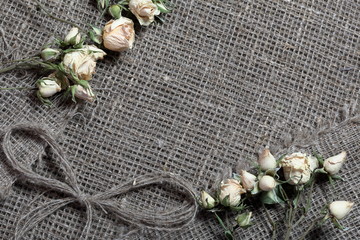 Coarse linen fabric. On it are dried beige roses and a bow of linen threads.