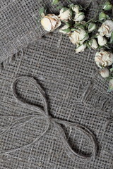 Coarse linen fabric. On it are dried beige roses and a bow of linen threads.
