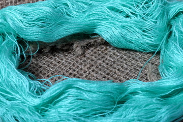 Coarse linen fabric. On it are hanks of green threads.