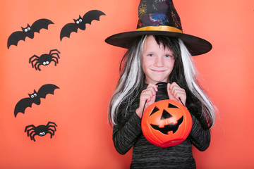 Fototapeta premium laughing child girl with pumpkins in witch costume on Halloween party. Halloween celebration concept, orange scary background with spiders and bats