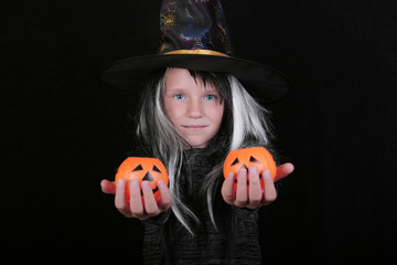 happy laughing child girl in witch costume with Halloween pumpkin candy jar on black background