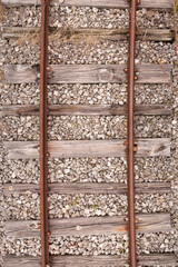 Top view of the old rusty rails with cracked wooden sleepers with a mound of small stones. Old vintage railway tracks