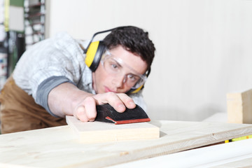 carpenter man work in the carpentry, sanding wooden boards with sandpaper, protected with ear muffs...