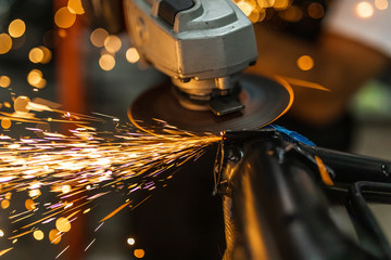Worker cutting, grinding and polishing motorcycle metal part with sparks indoor workshop, close-up.