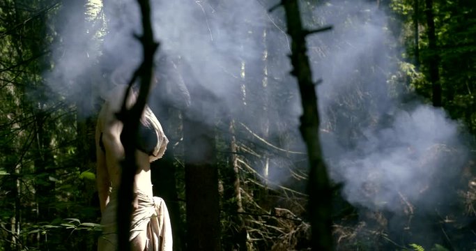 young woman dressed like ancient wild shaman is walking alone in forest in daytime