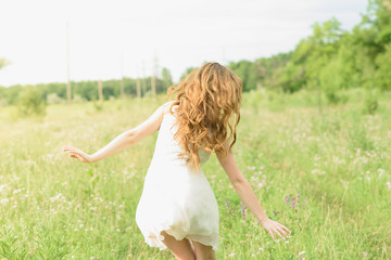Naklejka na ściany i meble Beautiful and happy young girl running on the green field in a white dress
