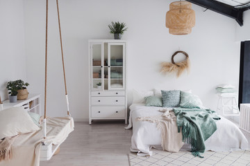 Modern scandinavian sunny bedroom with plants , white bedding and pillows. Space with white walls...