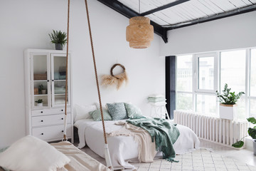 Modern scandinavian sunny bedroom with plants , floral pattern bedding and pillows. Space with white walls and wide window. Eco decor. Real photo.