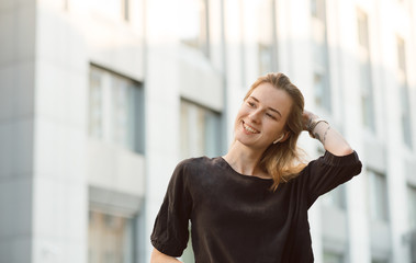 Portrait of smiling young girl in wireless headphones near the business center. Attractive woman with broad smile enjoying music in the earphones in modern city distrisct.