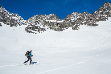 Backcountry skiing in the Talkeetna Mountains of Alaska. Skier moving uphill under large cliff bands in Hatcher Pass area.