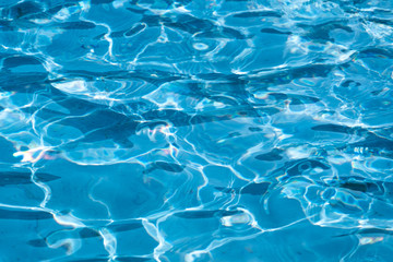 Blue and bright ripple water surface in swimming pool with sun reflection.