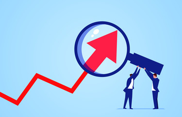 Two businessmen use magnifying glass to magnify arrows