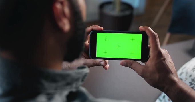 Male sitting indoors and holding prekeyed smartphone horizontally, template for advertisement
