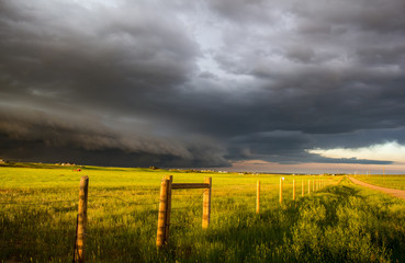 Fototapeta na wymiar A dark shelf cloud and storm approach as the sun shines brightly looking down a fence in the rural countryside.
