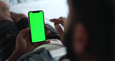 Young male lying on bed and touching chromakey smartphone, surfing internet, modern technologies