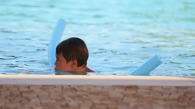 Little boy at the swimming pool holding into noodle float