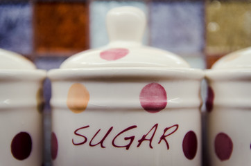Ceramic sugar pot against glass tile square background in the kitchen.