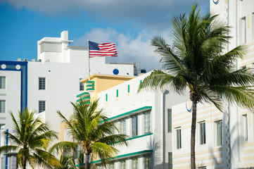 Sunny scenic view of American flag flying atop typical Art Deco architecture with tropical palm trees on Ocean Drive in South Beach, Miami, Florida