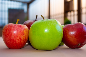 A group of red and one green apples in the front on top of the table with a colorful background.