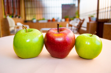 Two green apples and a red apple in the center seen from the front with a beautiful garden in the background.