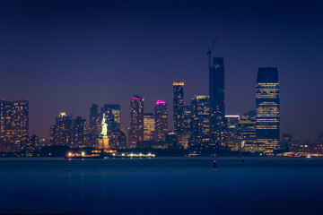 Statue of Liberty illuminated with lights at dusk after sunset in New York City, view from New York Bay