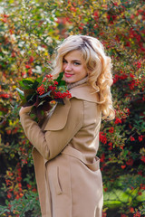 Beautiful elegant woman standing next barberry bush in autumn park