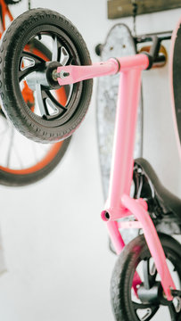 A pink toddler children's bike hanging on the wall. Apartment minimalism style of storing bicycle.