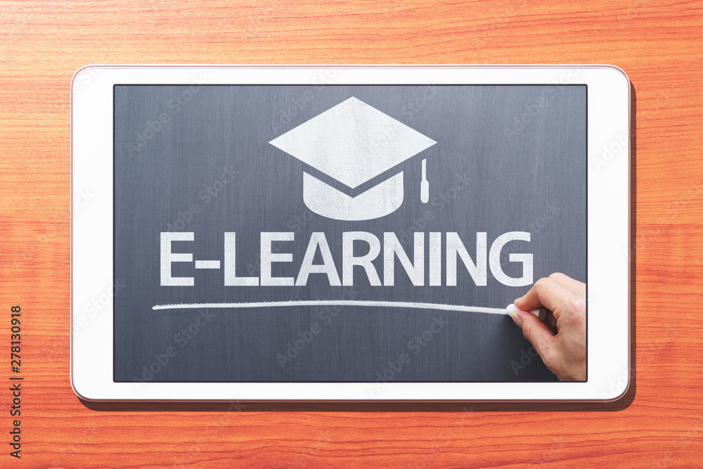 Poster E-learning concept. Tablet computer on wooden desk. Teacher writing on blackboard. Front view image.