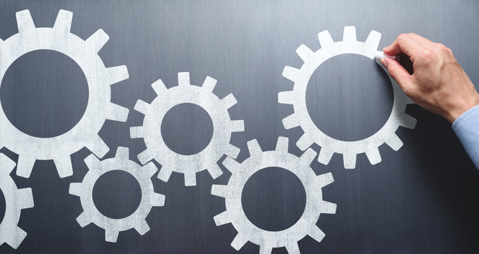 Business operation. Businessman drawing gears on chalkboard.