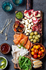 Antipasto. Wine set appetizer. Ham serrano, smoked salmon, dried and fresh tomatoes olive cheese, wine on board. Top view, gray cncrete background