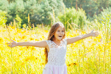 Little girl with long hair in a white dress rejoices in a field with flowers
