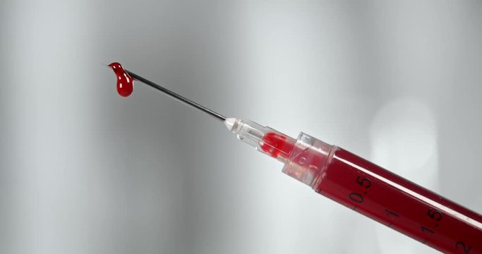 Syringe filled with blood and dripping from the needle