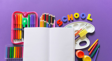 An open notebook lies on a Violet background. Around office supplies are the color of the rainbow.