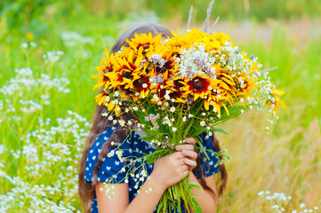 Little adorable girl gathered a bouquet of wild flowers