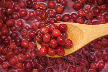 A man mixes a wooden spoon cherry jam.