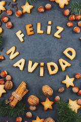 FELIZ NAVIDAD COOKIES. Words Merry Christmas en Spanish with baked cookies, Christmas decoration and nuts on black slate background.