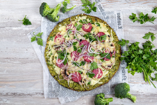 Crust Broccoli base low carbs keto pizza with salami, avocado on vintage newspapper. Top view