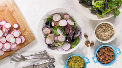  Herb Mix Salad with Fresh Organic Radish, Lettuces, Spinach, Some Seasoning, Almonds and Vegetable Oil. Close Up on White Background, Woman Hands