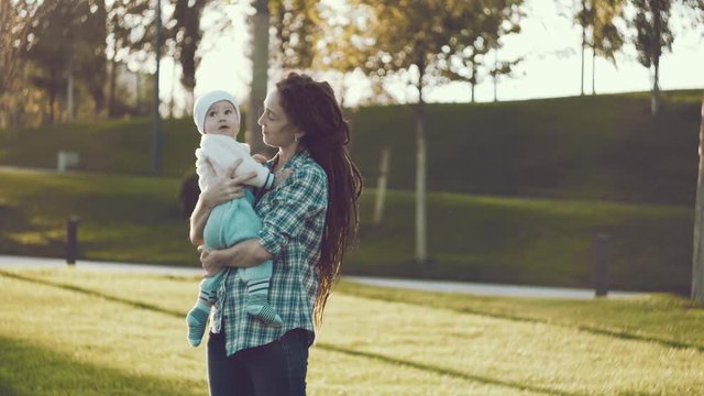 Modern happy mother with baby son in ergo backpack walking in Sunny summer day. Concept of the joy of motherhood