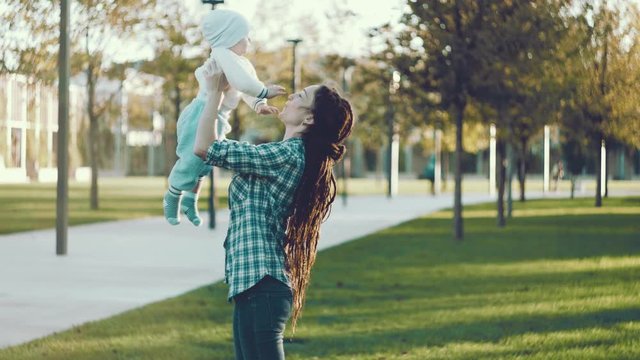 Modern happy mother with baby son in ergo backpack walking in Sunny summer day. Concept of the joy of motherhood