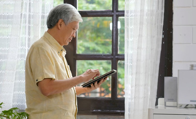 Senior asian man using digital tablet computer at home background, Retirement asian man and digital tablet standing by home window, Active senior people and technology lifestyles