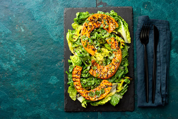 Grilled pumpkin salad with lettuce on black board plate, blue slate background. Autumn menu. Top view.