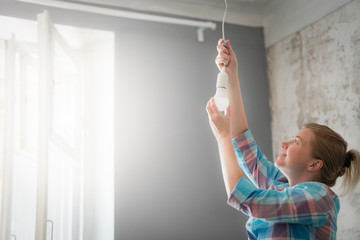 A woman changes the lamp in the pendant lamp.